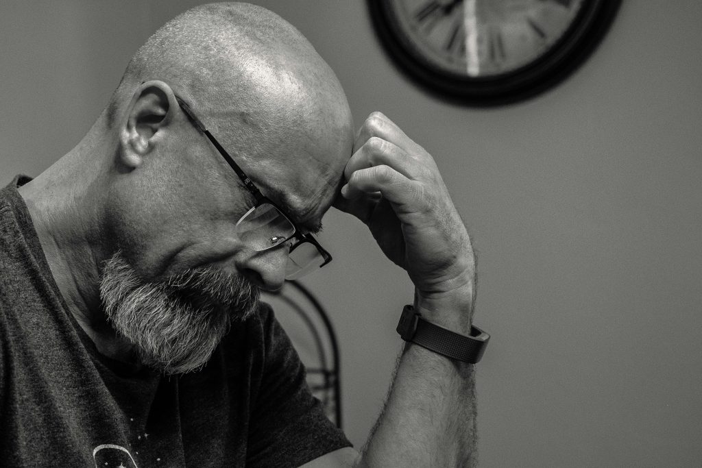 Black and white portrait of a thoughtful bald man indoors, capturing a moment of reflection with a wall clock in the background.